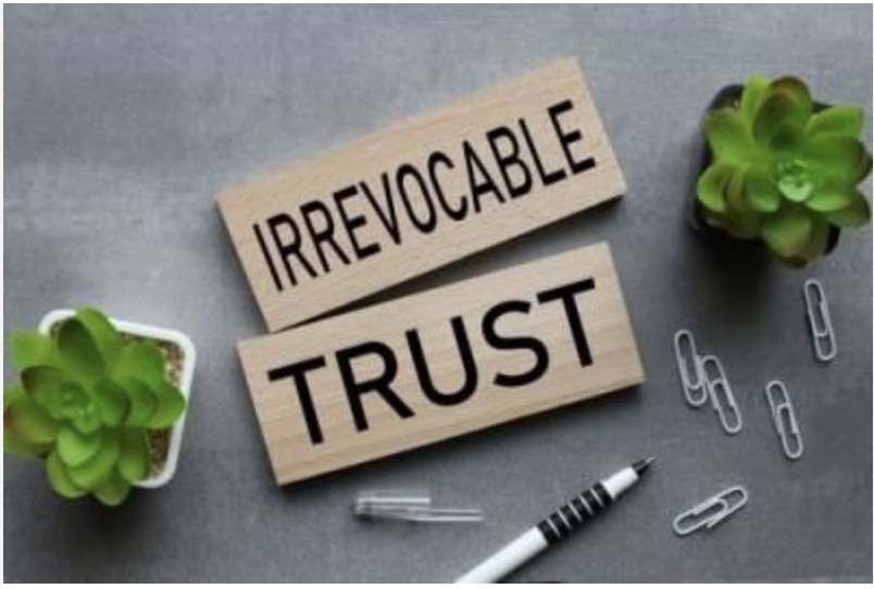 Two wooden signs reading 'IRREVOCABLE TRUST' on a desk with a pen and paper clips — representing the legal decision behind an irrevocable living trust