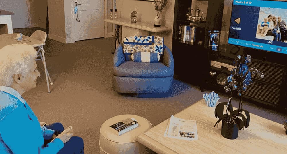 An older woman in a comfortable living room smiling at family photos on the OdessaConnect TV portal
