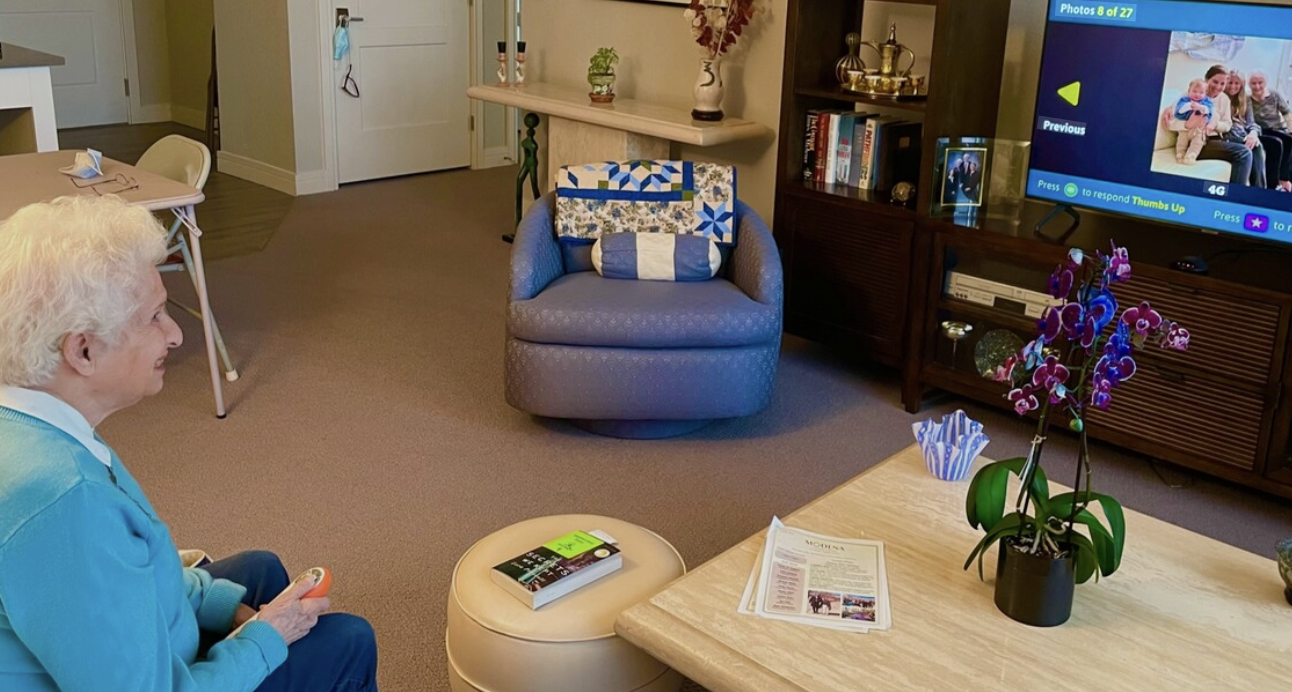 An older woman in a comfortable living room smiling at family photos on the OdessaConnect TV portal